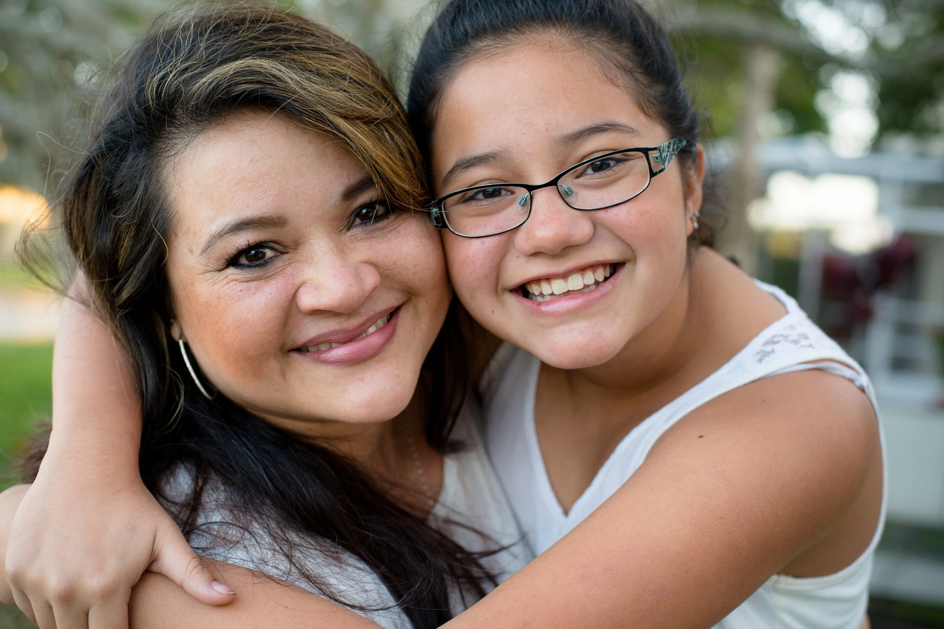 Latina mom and her tween daughter smiling and hugging each other.