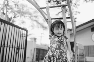 Six year old Asian girl hanging from the monkey bars at school. Photo in black and white.
