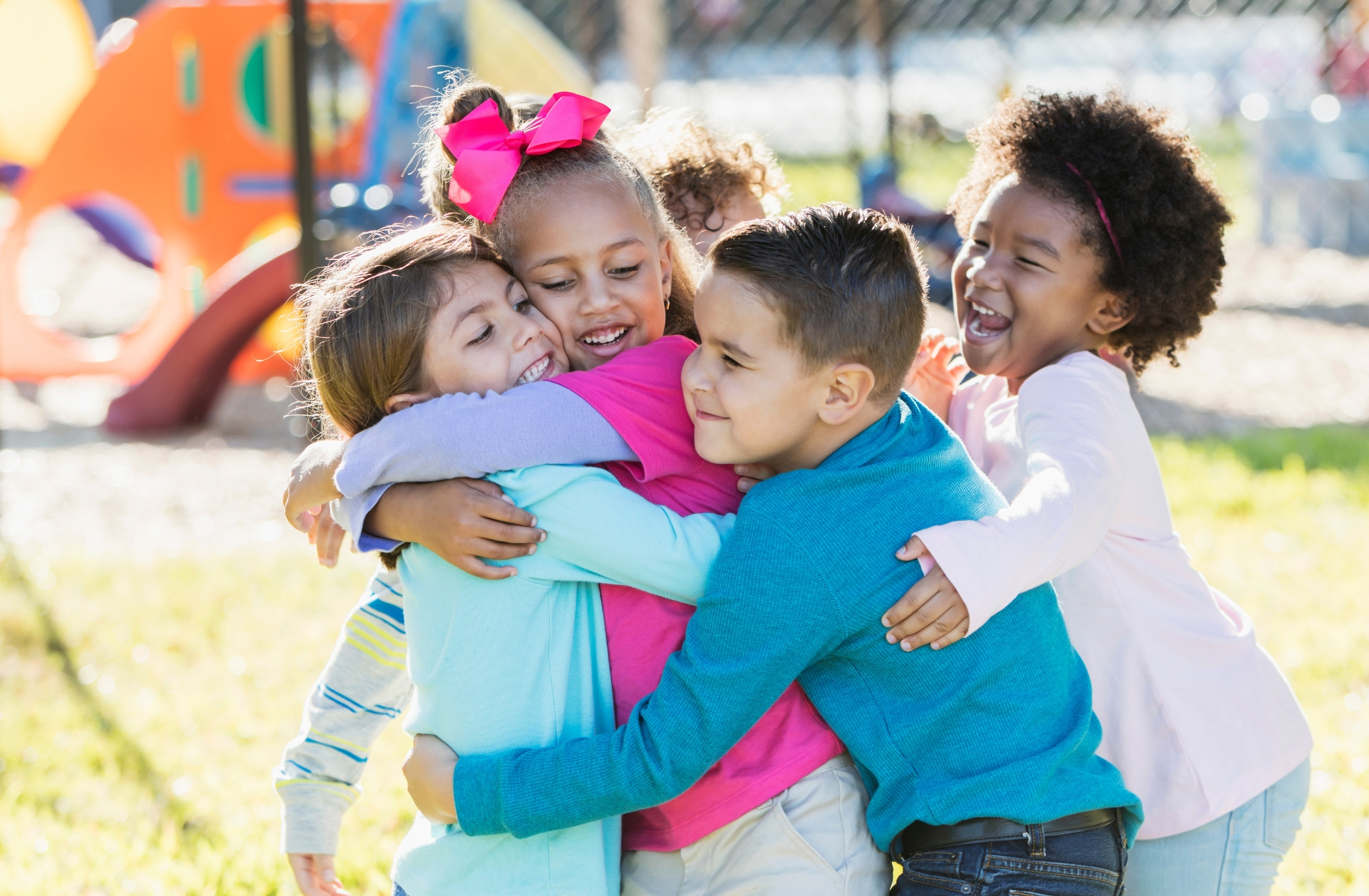 A group of children of color at a playground and joyfully participating in a group hug.