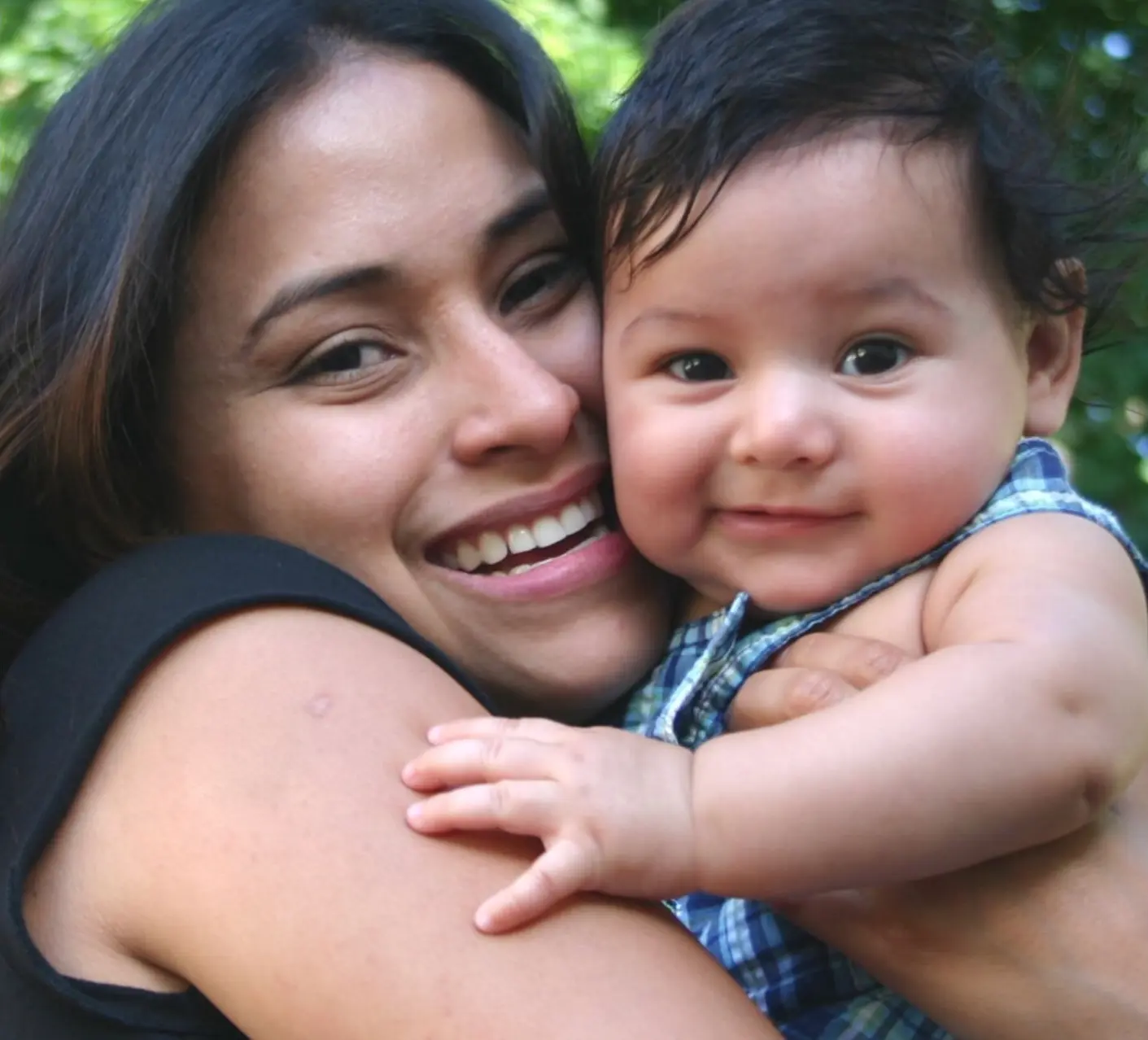 A Latina mother smiling and holding her baby boy close.