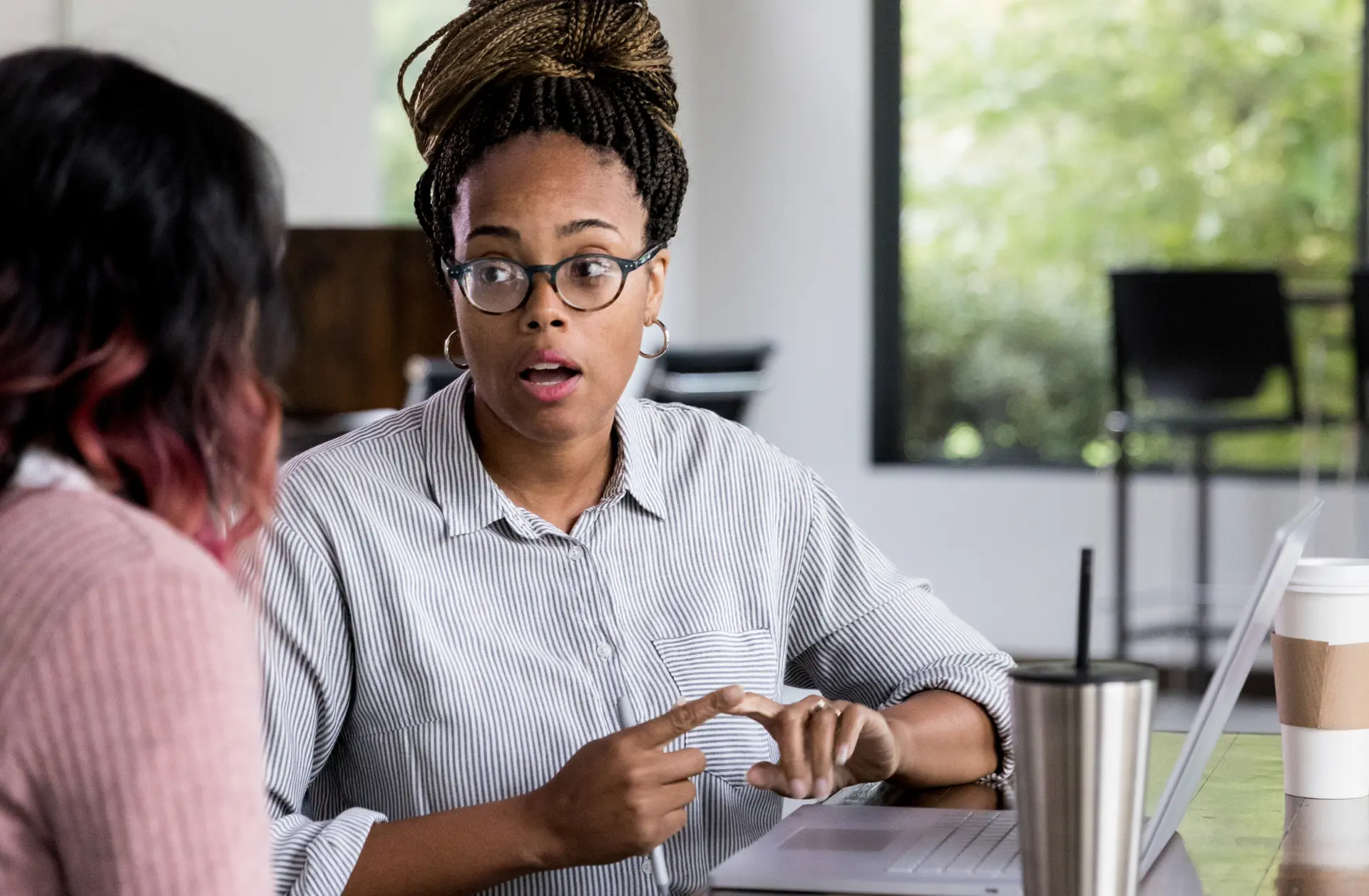 A Black woman wearing glasses talking with another woman in an office.