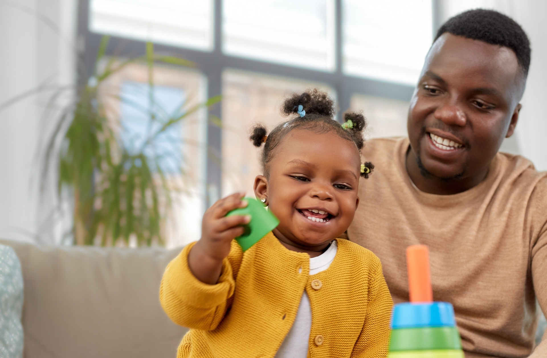 An African American father playing blocks with his daughter. She's wearing Bantu knots and a mustard yellow sweater.