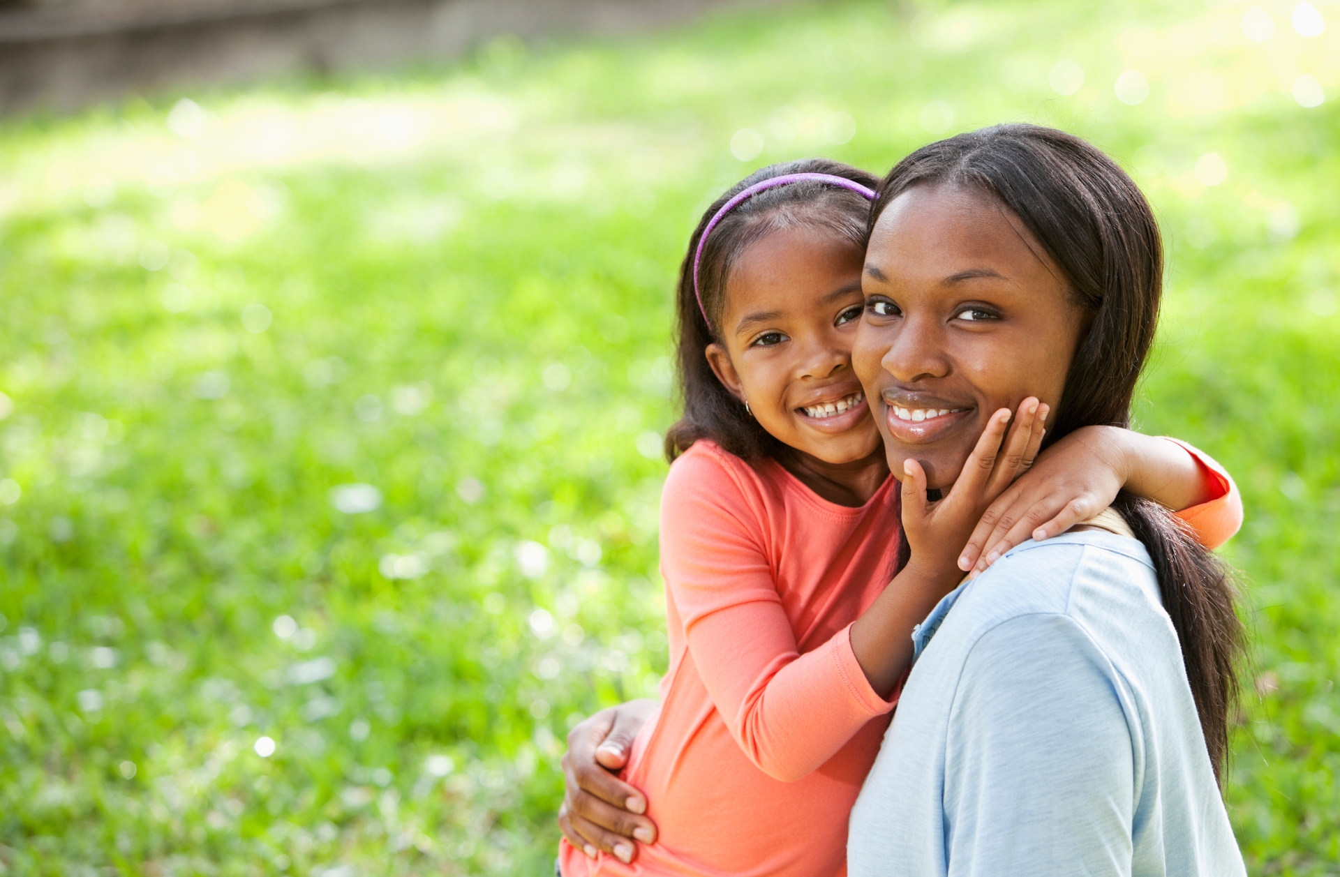 An African American mother and daughter hugging outside.