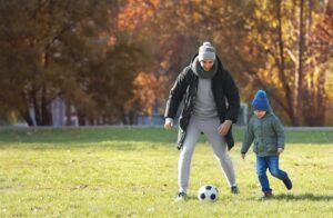 Father and son playing soccer outside in the autumn.