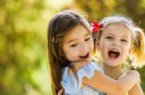 Two little girls, both have fair skin, playing and laughing while holding each other.