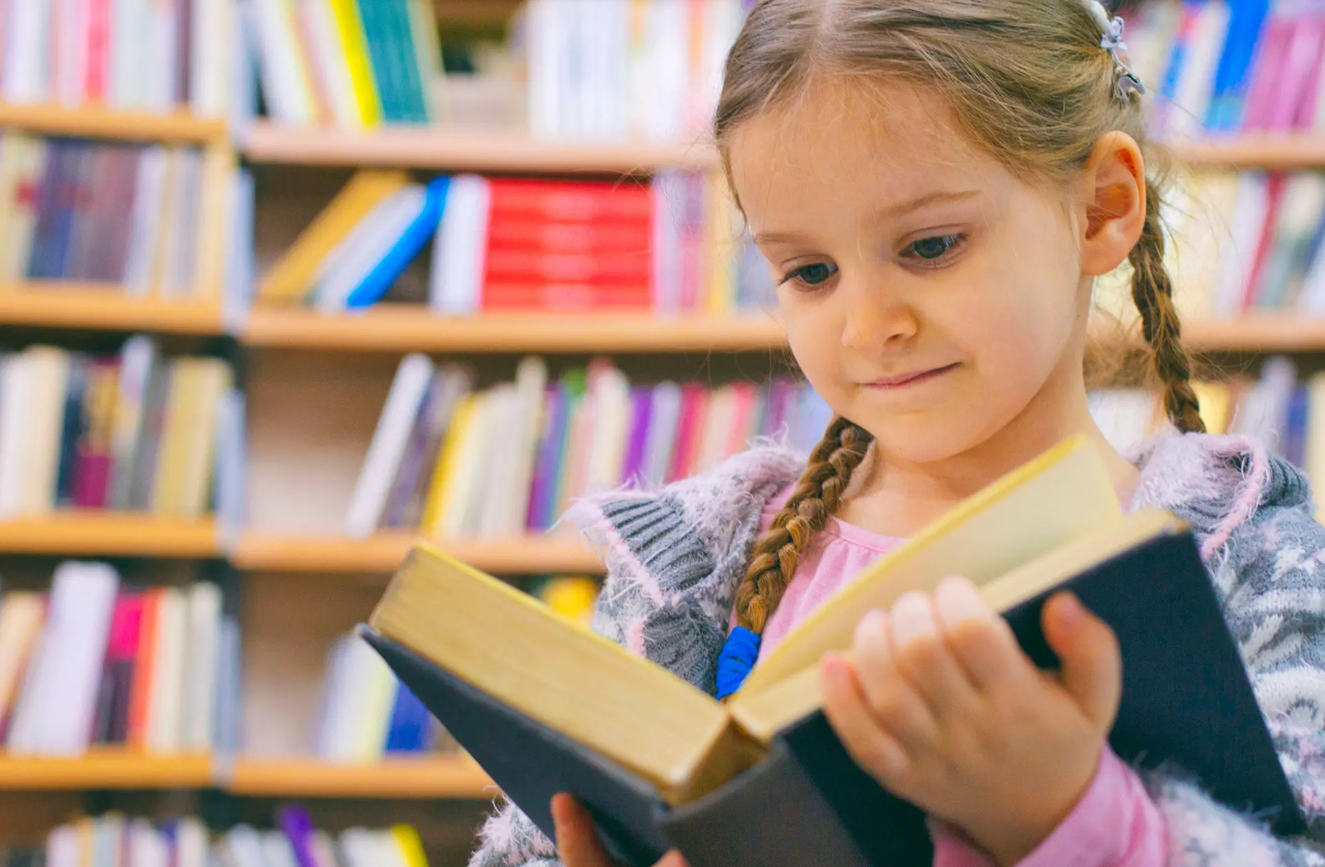 A young girl reading a book at the library.